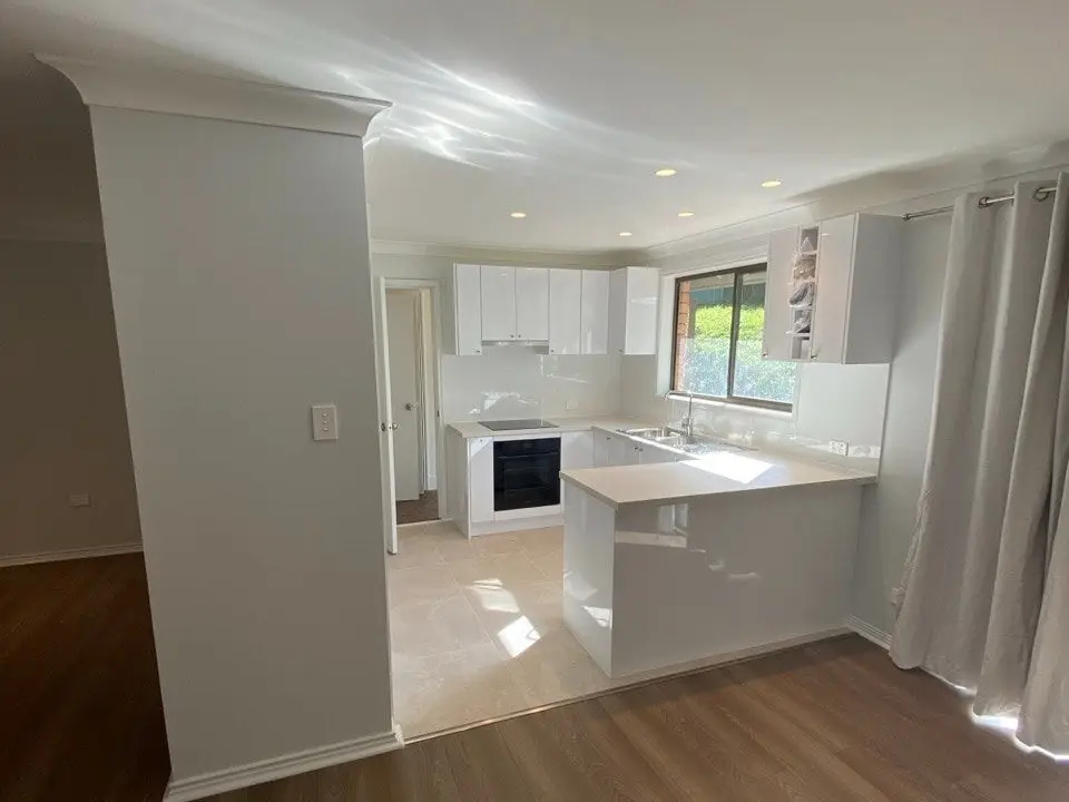 Renovated kitchen with white cabinetry, stone benchtop and timber-look floor, by Trusted